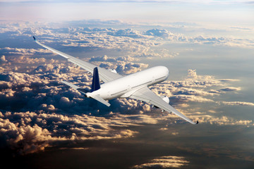 The passenger plane flies away beyond the horizon. The plane flies over the clouds during the sunset. Rear view of aircraft.