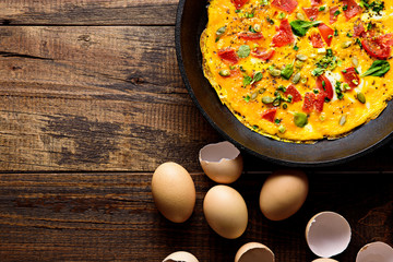 top view rustic Breakfast, scrambled eggs with greens, tomatoes and pumpkin seeds on brown wooden background with copy space