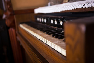 Selective focus on the keyboard on an old rustic piano. There are lace tablecloths on the piano. The piano is very old and quite used.