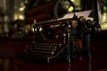 An old black rustic typewriter is on a desk in a 19th century office and ready to be worked on.
