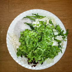 the white plate of vegetables and grass noodle and some mushrooms for put in the soup, in Thailand called this kind of soup is 