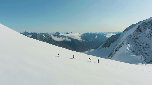 Group of Alpinists is Advancing as Roped Team in Snowy Mountains on Sunny Day. European Alps. Aerial View. Drone is Orbiting