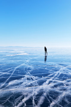 Naklejki Frozen Baikal Lake in February. The endless desert of blue ice with a crack. A lone tourist skates on ice in the distance. Winter landscape. Natural background