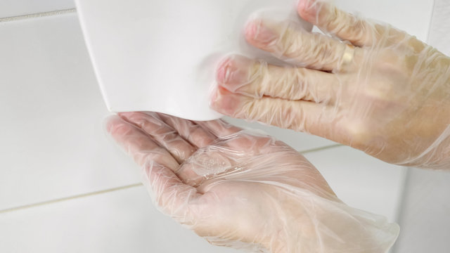 woman hands in rubber gloves push wall mounted antiseptic dispenser button and get clear sanitization gel closeup