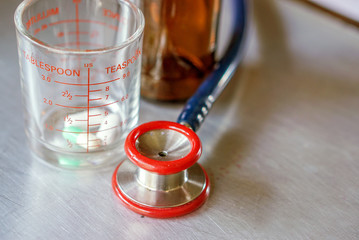 Closeup and crop  Small doctor stethoscope  with medicine in medical glass and Brown medicine bottle on aluminum board.