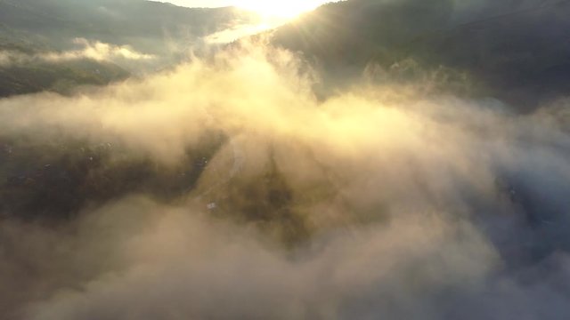 Flying through beautiful sunny cloudscape in the mountains at sunrise. Aerial view of above mountain tops