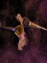closeup cosmetic brush releasing a cloud of sparkling powder over a black background 
