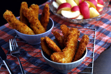 Freshly cooked crispy chicken and fish strips and bowl of sliced apple and pear