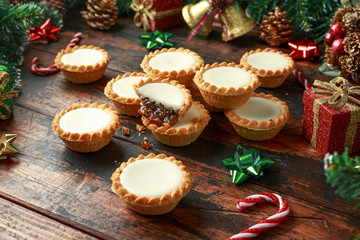 British Christmas iced mince pies with decoration, gifts, green tree branch on wooden rustic table