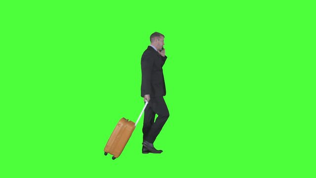Handsome Caucasian entrepreneur walking in the studio while carrying a suitcase and making a phone call. Shot in 4k resolution with green screen background