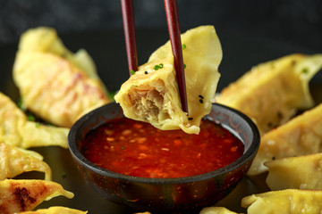 Chopsticks holding and dipping meat dumplings, fried yaki gyoza in sweet chilli sauce.