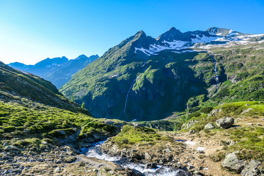 A view on Schladming Alps, partially still covered with snow. A small stream flowing between the stones. Spring slowly reaching the tallest parts of the mountains. First sunbeams reaching the peak.