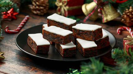 Christmas iced fruit cake with decoration, gifts, green tree branch on wooden rustic table