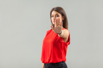 Stop! Portrait of serious beautiful brunette young woman in red shirt standing with stop hand sign...