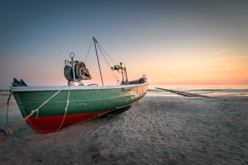 Naklejka na ściany i meble Old abandoned fishing boat at Latvia beach at sunset with colorful sky