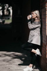 beautiful blonde woman in a gray coat on a walk in the city with a plastic cup of coffee