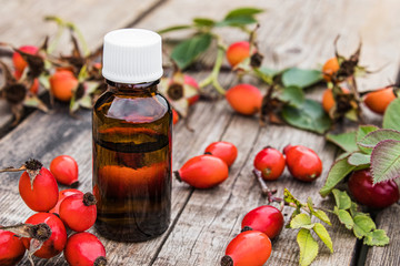 Bottle of rosehip seed essential oil and fresh red berries on a wooden table. Tincture or essential oil with rose hips.