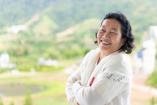 Asian elderly woman wear a white cloth is standing and smiling in the background of green mountain background, concept of happy and healthy of senior asian people.