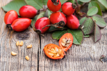 Red rose hips and ripened berries in half with seeds on old wooden boards.