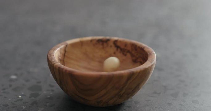 Slow motion peeled macadamia nuts fall into olive wood bowl
