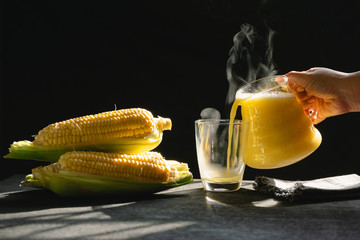 The steam from a jug and a glass of corn milk on black background, Warm drinks make good...