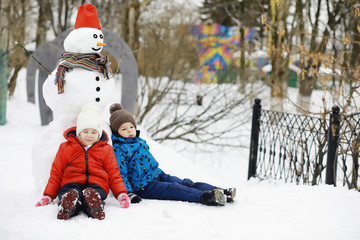 Fototapeta na wymiar Children in the park in winter. Kids play with snow on the playground. They sculpt snowmen and slide down the hills.
