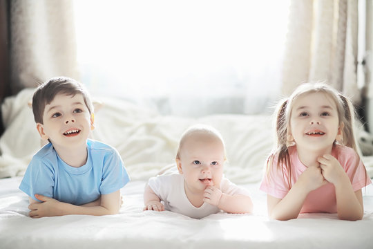 Children lie on the bed next to the newborn baby, little sister.