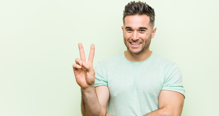 Naklejka premium Young handsome man against a green background showing number two with fingers.