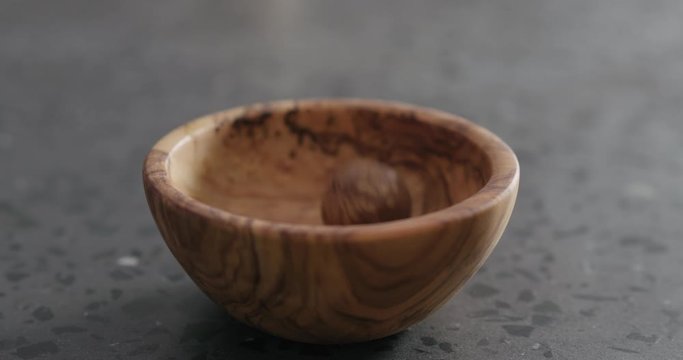 Slow motion inshell macadamia nuts fall into olive wood bowl