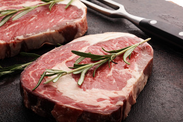 Raw fresh meat Ribeye Steak, seasoning and meat fork on rustic background