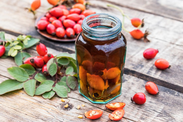 Tincture or drink with wild rose in a glass bottle near ripe red rosehip berries.