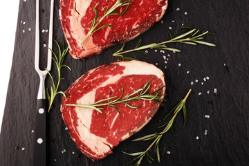 Raw fresh meat Ribeye Steak, seasoning and meat fork on rustic background