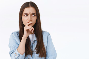 Pensive, serious-looking focused caucasian woman in denim jacket, touching lip thoughtful, frowning intense and looking sideways as thinking, having troublesome thoughts, white background