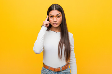 Young pretty arab woman against a yellow background pointing temple with finger, thinking, focused...