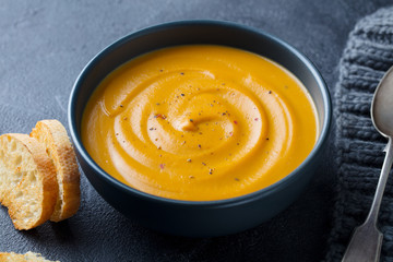 Pumpkin, carrot cream soup in a bowl. Grey background. Close up.