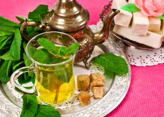 Moroccan tea in a glass with green mint, dessert on a pink textile background
