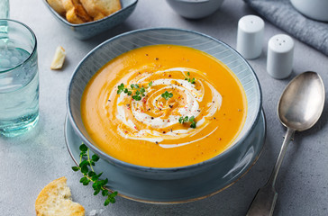 Pumpkin and carrot soup with cream on grey stone background. Close up.