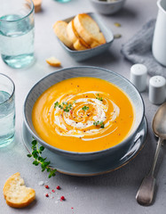 Pumpkin and carrot soup with cream on grey stone background.