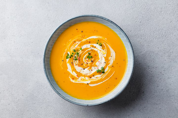 Pumpkin and carrot soup with cream on grey stone background. Top view.
