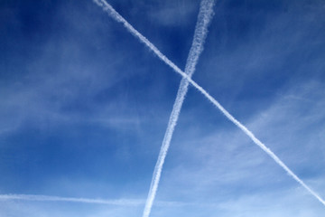 Multiple aiplane trails, chemtrails or jet trails over blue sky background