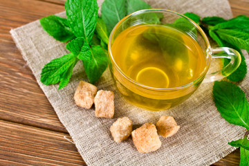 Cup of green tea with brown sugar and fresh mint leaves on a wooden background. Top view.