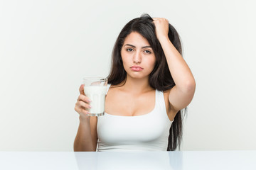 Young hispanic woman holding a glass of milk being shocked, she has remembered important meeting.