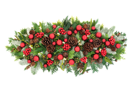 Christmas festive table decoration with red baubles, winter holly, snow covered fir, mistletoe, ivy, pine cones and cedar leaves on white background with copy space. Flat lay, top view..