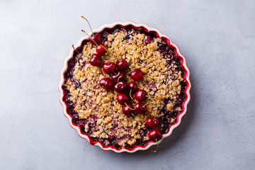 Cherry, red berry crumble in baking dish. Grey stone background. Top view.