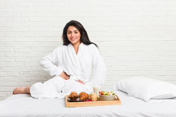 Young curvy woman taking a breakfast on the bed confident keeping hands on hips.