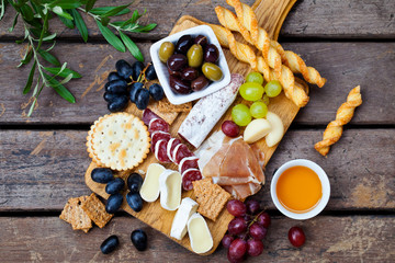 Cheese and meat appetizers on cutting board on wooden background. Top view.