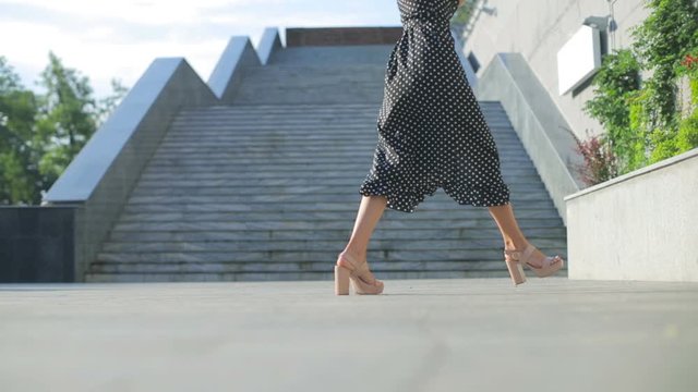 beautiful lady in high heels shoes walks and dances shaking hands against grey concrete stairs low angle shot