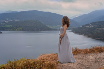 Beautiful girl in long romantic grey dress look on the Scenic landscape Germasogeia reservoir large artificial lake staying on dam during a sunset under dramatic cloudy sky, Limassol district, Cyprus