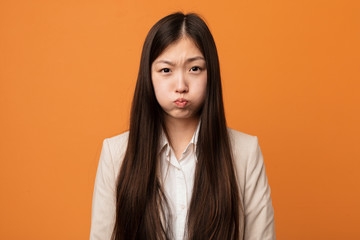 Young business chinese woman blows cheeks, has tired expression. Facial expression concept.