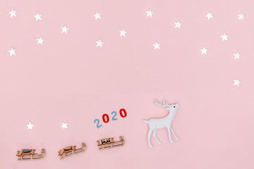 New year 2020, Christmas frame, greeting card. White stars, deer with Santa's sleigh on pastel pink paper background. Top view, flat lay, copy space